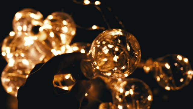 Hand Holds a Light Bulb on the Background of a Garland of Glowing Light Bulbs