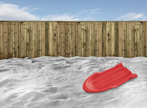 Red plastic toboggan on a snow in a backyard with a fence