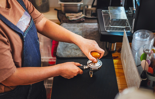 Barista holding portafilter and coffee tamper making an espresso coffee in coffee shop