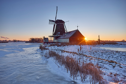 Old windmill in winter during sunrise, Zaandijk, The Netherlands. The water is frozen en covered with snow.