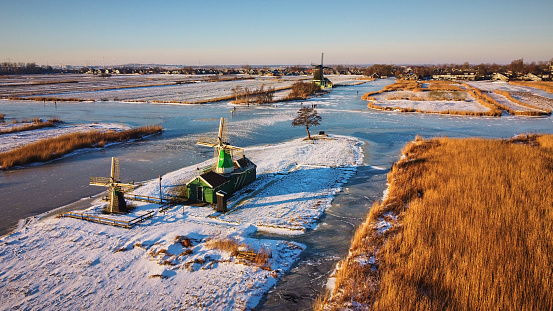 Aerial of the polder with old windmills during sunrise in the winter, Zaandijk, The Netherlands everything is covered with snow and the water is al frozen.
