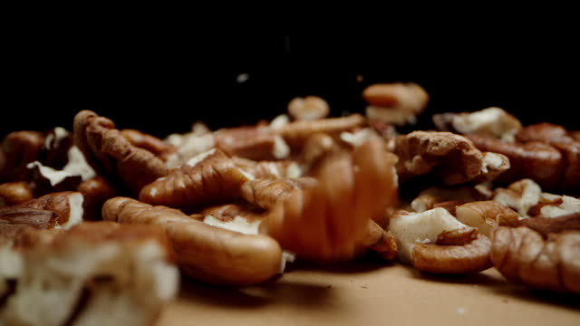 Peeled pecan nuts fall onto the table against a black background, close-up, slowed down.