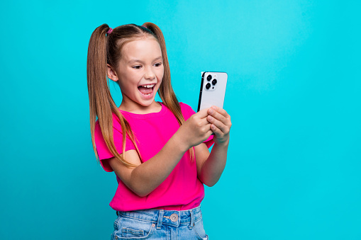 Portrait of funny optimistic little girl dressed pink t-shirt recording video on smartphone isolated on turquoise color background.