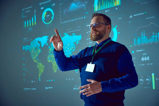 istock Speaker, lecturer stands near presentation board with graphs, maps and pointing up drawing audience's attention to important details in his speech 2065766631
