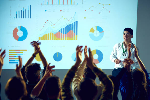 business training session surrounded by data visualizations where man ending speech and audience clapping raising hands. - training business seminar clapping imagens e fotografias de stock