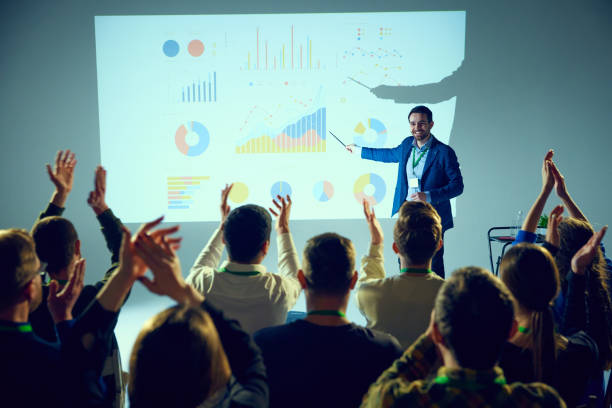 corporate training lecture surrounded by data visualizations where man ending speech and audience clapping raising hands. - training business seminar clapping imagens e fotografias de stock