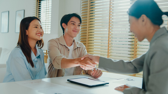 Asian female real estate agent handshaking after signing a complete agreement with tenants after showing new houses. Landlord selling real estate to happy couple customer for investment concept.
