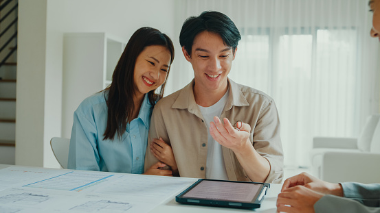 Asian female real estate agent giving house key after signing agreement of new houses with tenants. Landlord selling real estate to happy couple customer for investment concept.