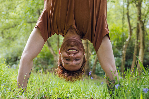 Close up of a young man doing a handstand during an outdoor solo yoga session in the forrest in Northumberland in the North East of England. He is working on his core and is feeling cheerful and serene in his peaceful surroundings.