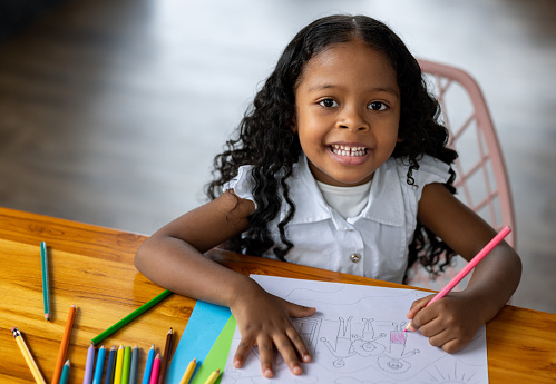 Happy African American girl coloring at home and looking at the camera smiling