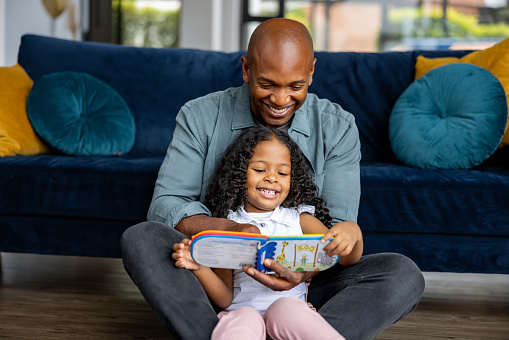Loving African American father reading a book to his daughter at home â lifestyle concepts