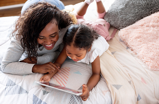 Happy African American mother reading a bedtime story to her daughter using a digital tablet