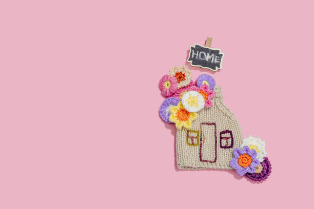 Handmade home spring decor concept. Creative crocheting, house figurine, traditional flowers. Festive greeting card, gentle pastel pink background, top view