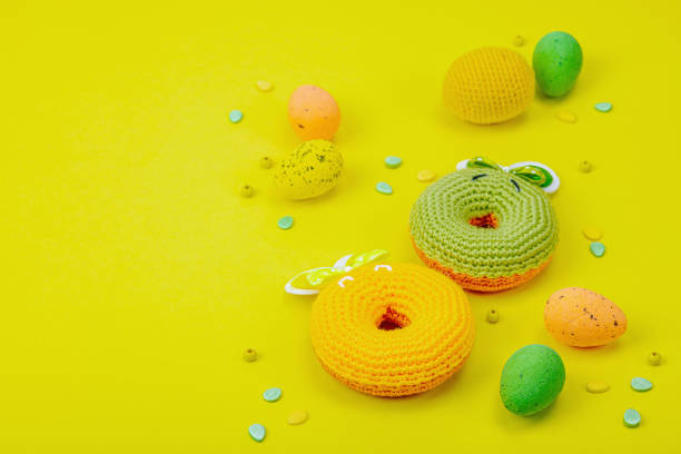 Handmade Easter concept. Crocheted donuts bunnies with traditional decoration. Festive symbols, greeting card, flat lay. Creative craft concept, bright yellow background, copy space