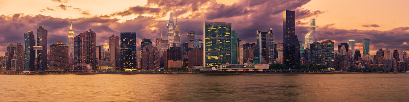 High Resolution Stitched Panorama of New York Skyline with UN Building (Headquarters of the United Nations), Chrysler Building, Empire State Building, Manhattan Upper East Side Residential and Office High-rises, FDR drive, water of East River, Green Trees and Sunset Magenta Blue Sky with Clouds. Canon EOS 6D (Full Frame censor) DSLR and Canon EF 85mm f/1.8 lens. 4:1 Image Aspect Ratio. This image is downsized to 50MP. The Original image resolution is 90MP or 18,923 x 4,731 px.