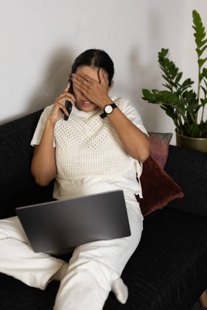 istock Disappointed woman working from home using laptop and smartphone sitting on couch 2065880434