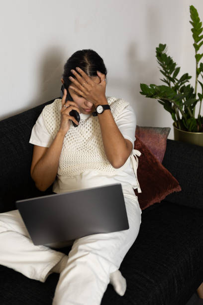 istock Disappointed woman working from home using laptop and smartphone sitting on couch 2065881977