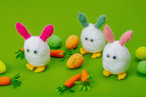 Handmade Easter concept. Knitted bunnies with traditional decoration. Festive symbols, greeting card, flat lay. Creative craft concept, bright green background, close up