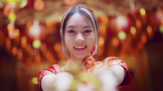 young asian girl in red Cheongsam gives you the gold ingot she is holding.smiling broadly and glancing at the camera.chinese new year concept.
