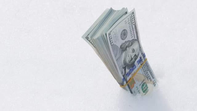 stack of hundred us dollar banknotes sticking out from snow