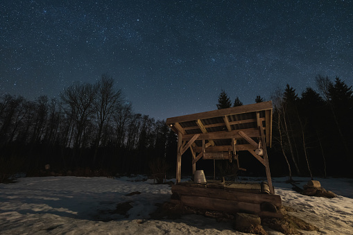 Night scene, landscape astrophoto, old well in the forest with a starry sky. High quality photo