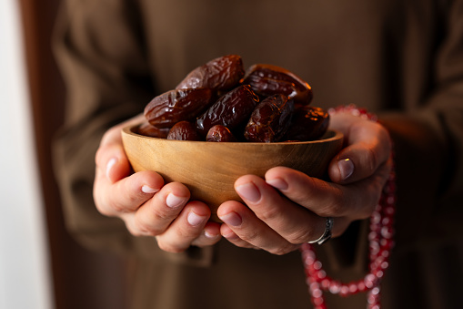Muslim woman holding dates fruit in a wooden bowl. Traditional Ramadan food.