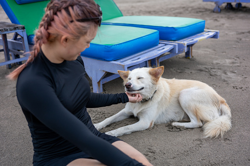 A young Asian woman is resting with her dog on the beach and sunbathing during her vacation at Seminyak Beach, Bali Island, Indonesia.