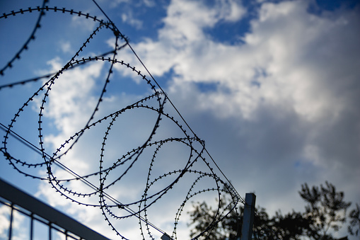Security fence with barbed wire against cloudy sky