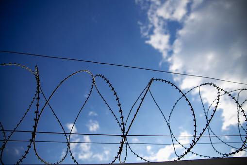 Security fence with barbed wire against cloudy sky