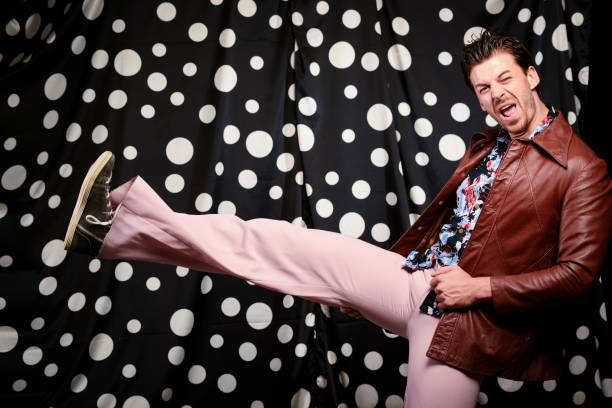 A senior East Asian man stands against a hot pink background, wearing a colorful shirt.