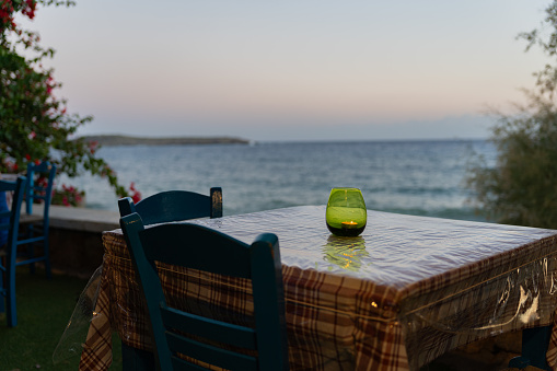 Beautiful photograph of table chairs in a Greek tavern with a lit candle and the Aegean Sea in the background at sunset