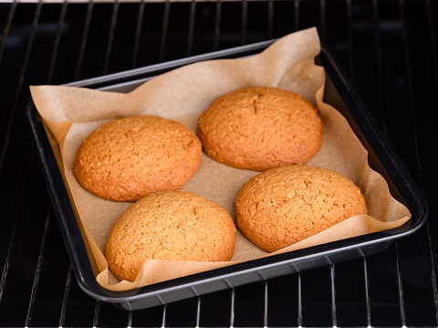 A baking tray with oatmeal cookies in it in an oven.