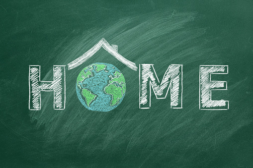 The word HOME written on a chalkboard with a house and globe symbol in place of the letter O. Planet Earth is our Home. Earth day concept.