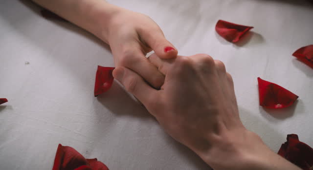 Lovers' hands touch each other surrounded by lying rose petals