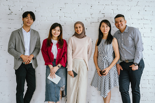 A small group photo of a multi-ethnic Asian business team standing tall, epitomizing togetherness as leaders of the business world after a successful business conference.