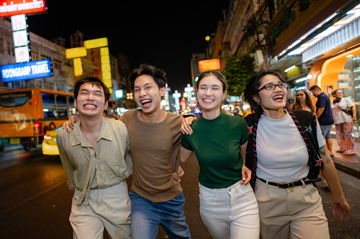Portrait of Asian friends explore street food while walking through the vibrant streets of Yaowarat Road at Night.