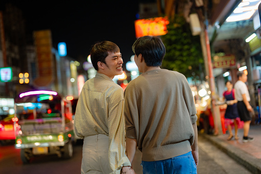 LGBTQIA couple explore street food while walking through the vibrant streets of Yaowarat Road at Night.