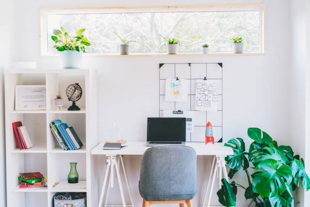 istock Modern cozy light workplace - white desk with laptop black screen, grid mood board with pinned notes, shelves with docs and green monstera plant at work space in home office room interior 2066127358