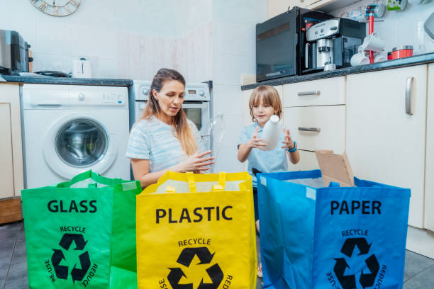 Mother is teaching kid how to recycle help the boy aware environmental importance - mom educates son sort garbage into different bins on kitchen. Family sorting garbage at home. Concept of recycling.
