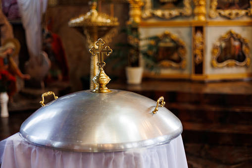 Aluminium church font, large bowl, with golden cross and saint water for the baptism of babies in Orthodox Church temple, Christening ceremony. Concept of rituals, sacraments of the Christian religion
