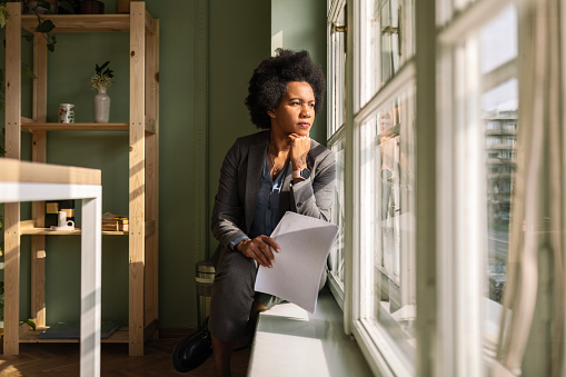 Businesswoman sitting on window sill with documents