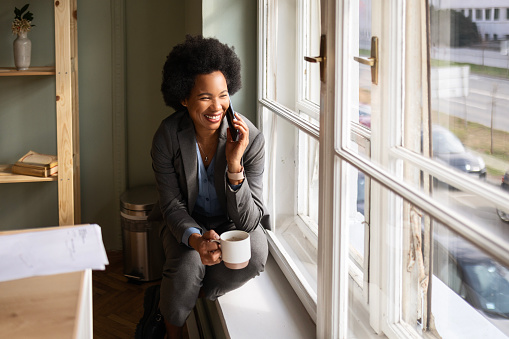 Businesswoman sitting on window sill with smart phone