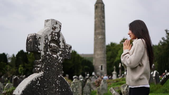 Beautiful young woman praying and mourning by tombstone at graveyard, View of Glendalough ruins in Wicklow Ireland, view of Glendalough abbey, view of Glendalough upper and lower lakes in Ireland, popular tourist destination in Ireland