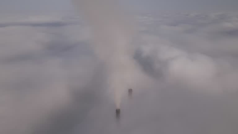 Coal power plant high pipes with black smoke moving upwards over clouds polluting atmosphere. Production of electrical energy with fossil fuel concept