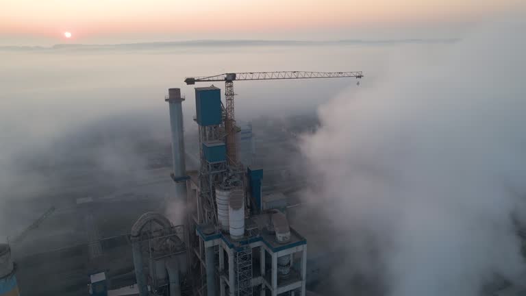 Cement factory with high concrete plant structure and tower crane at industrial manufacturing site on foggy evening. Production and global industry concept.