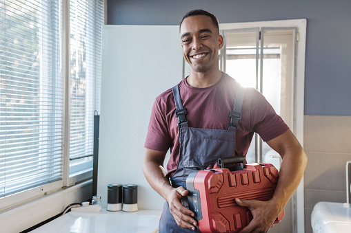 Photo of African American handyman holding tool box while standing in the customer's kitchen