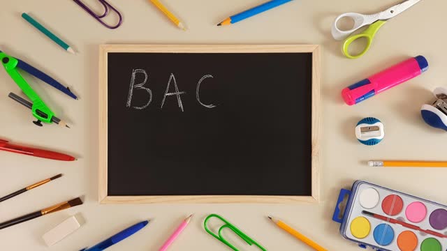 Back to school chalk text appears on a school black board on a neutral pastel background with stationery.