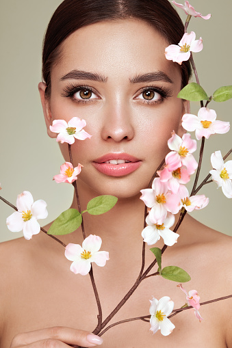 Beautiful young woman with a cherry blossom branch. Model with clean fresh skin, close up portrait. Cosmetology, facial skin care, beauty and spa