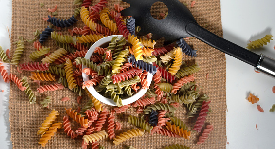 Colorful pasta spread on a table next to utensils.