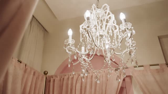 A  Cozy Bedroom with a Crystal Chandelier Suspended Overhead - Low Angle Shot